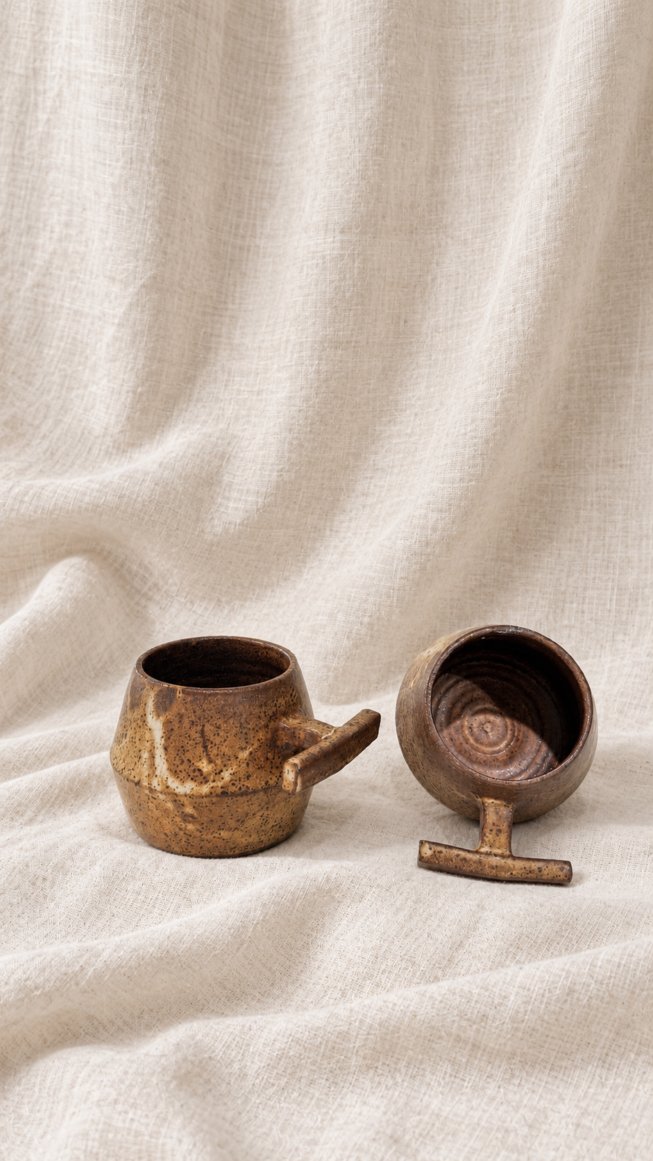 Death Valley handmade ceramic mugs with brown and ochre glaze, dark speckles and sculptural handles on offwhite linen