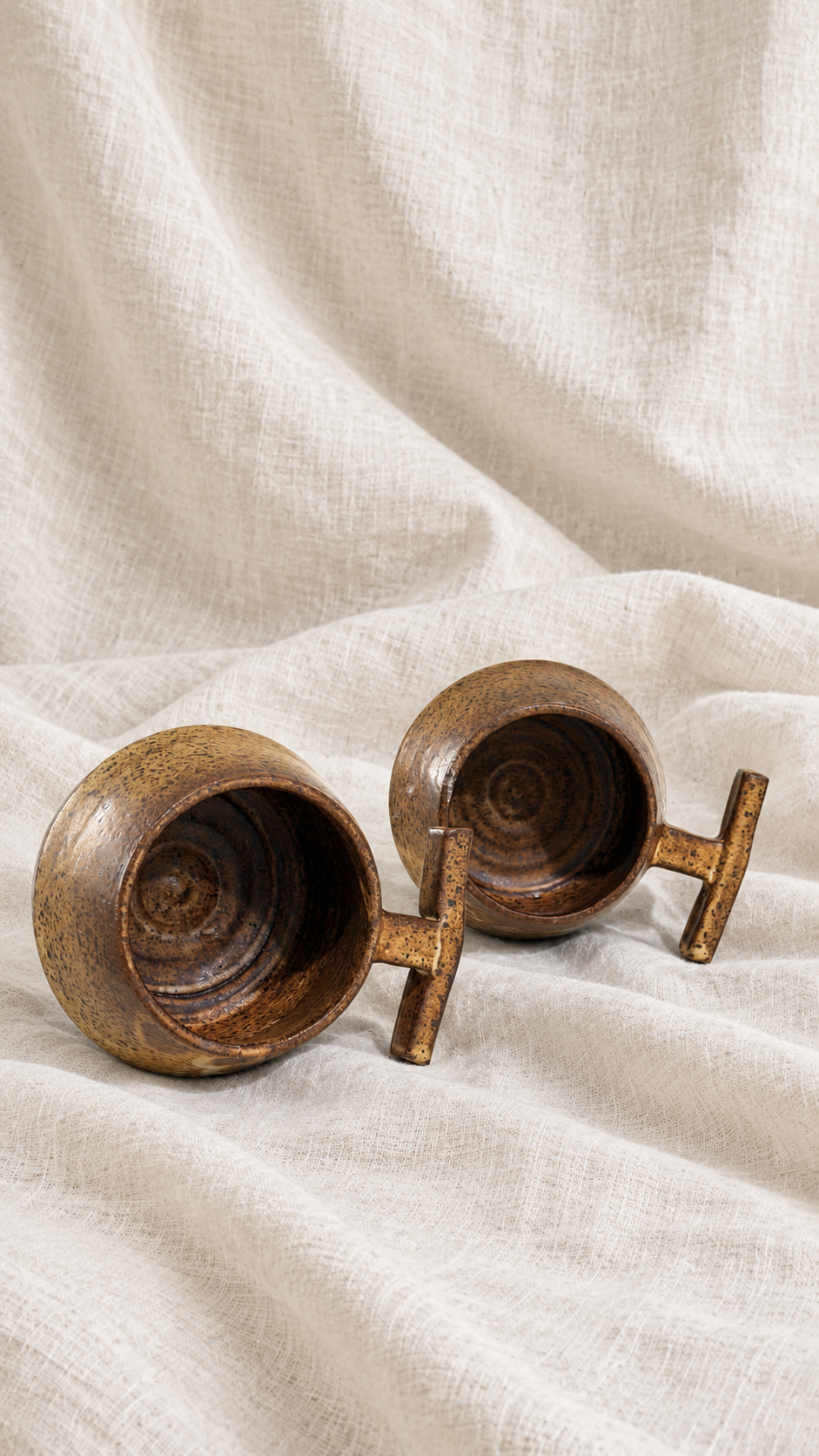 Death Valley handmade ceramic mugs with brown and ochre glaze, dark speckles and sculptural handles on offwhite linen